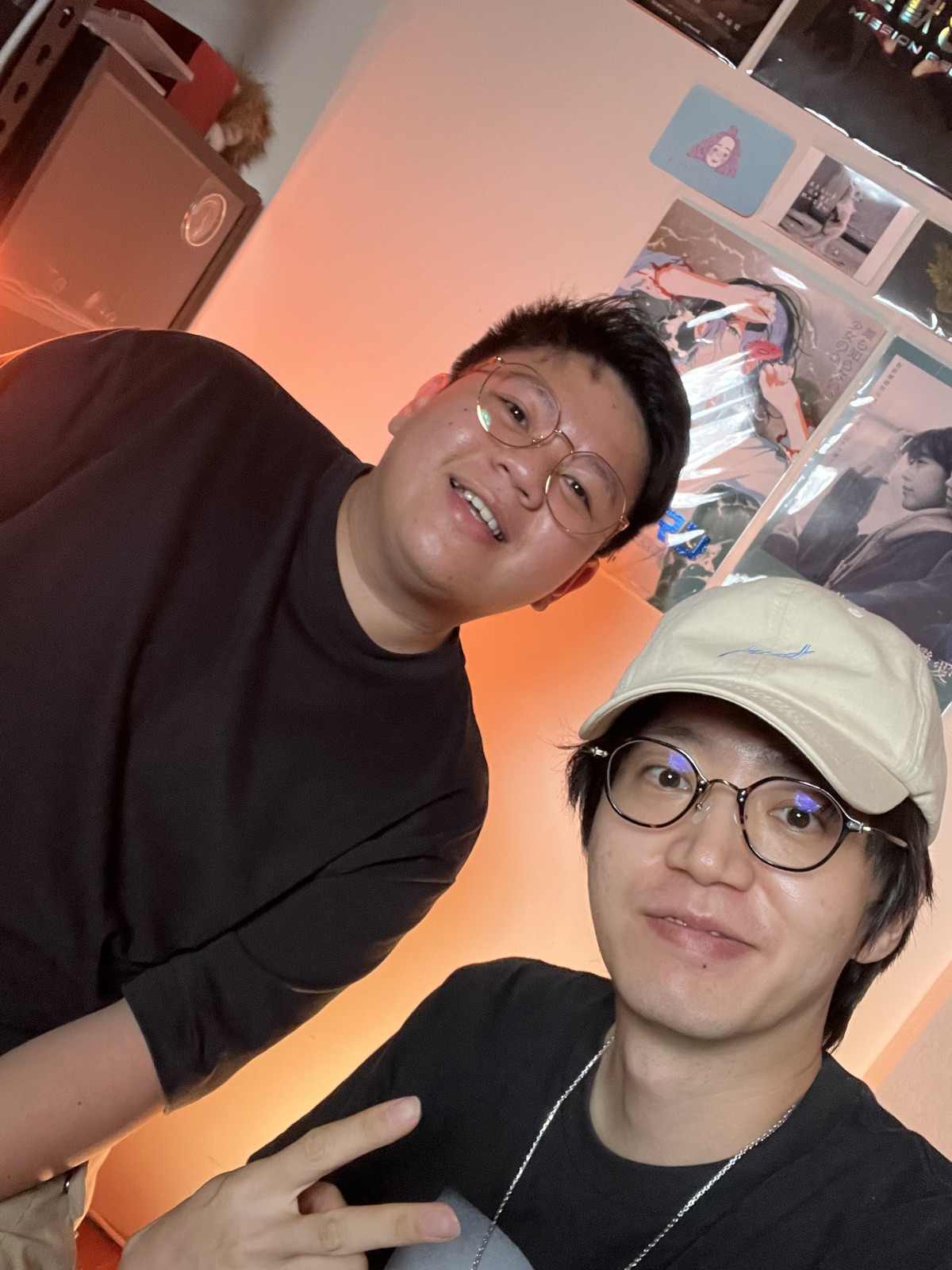 暖橘燈光的工作室裡兩個人臉靠著臉看向鏡頭合照,牆上貼著海報。