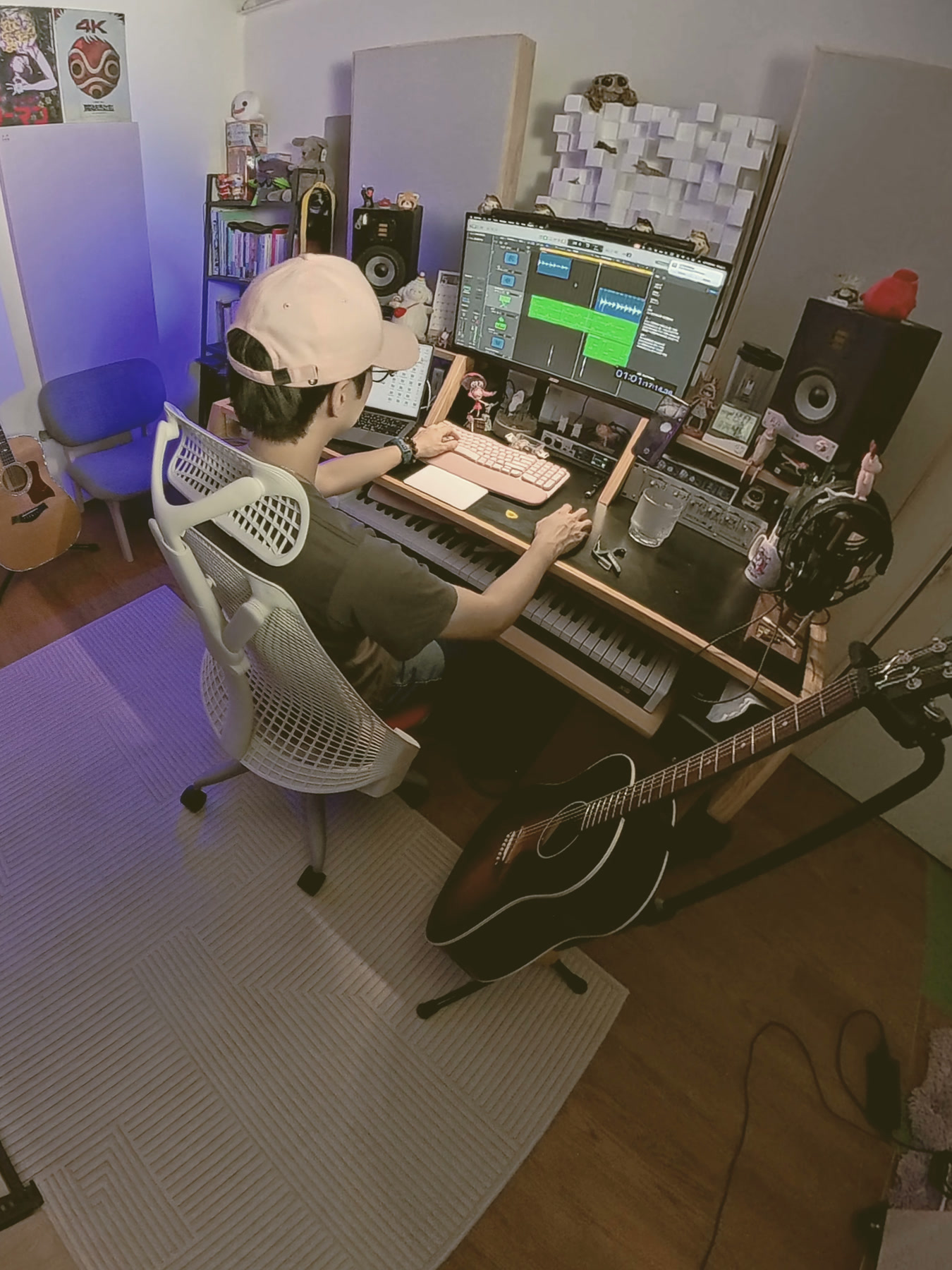 五分熟音樂工作室:小羊坐在工作桌前編曲,桌上有主控鍵盤與監聽喇叭,前景立著一把木吉他